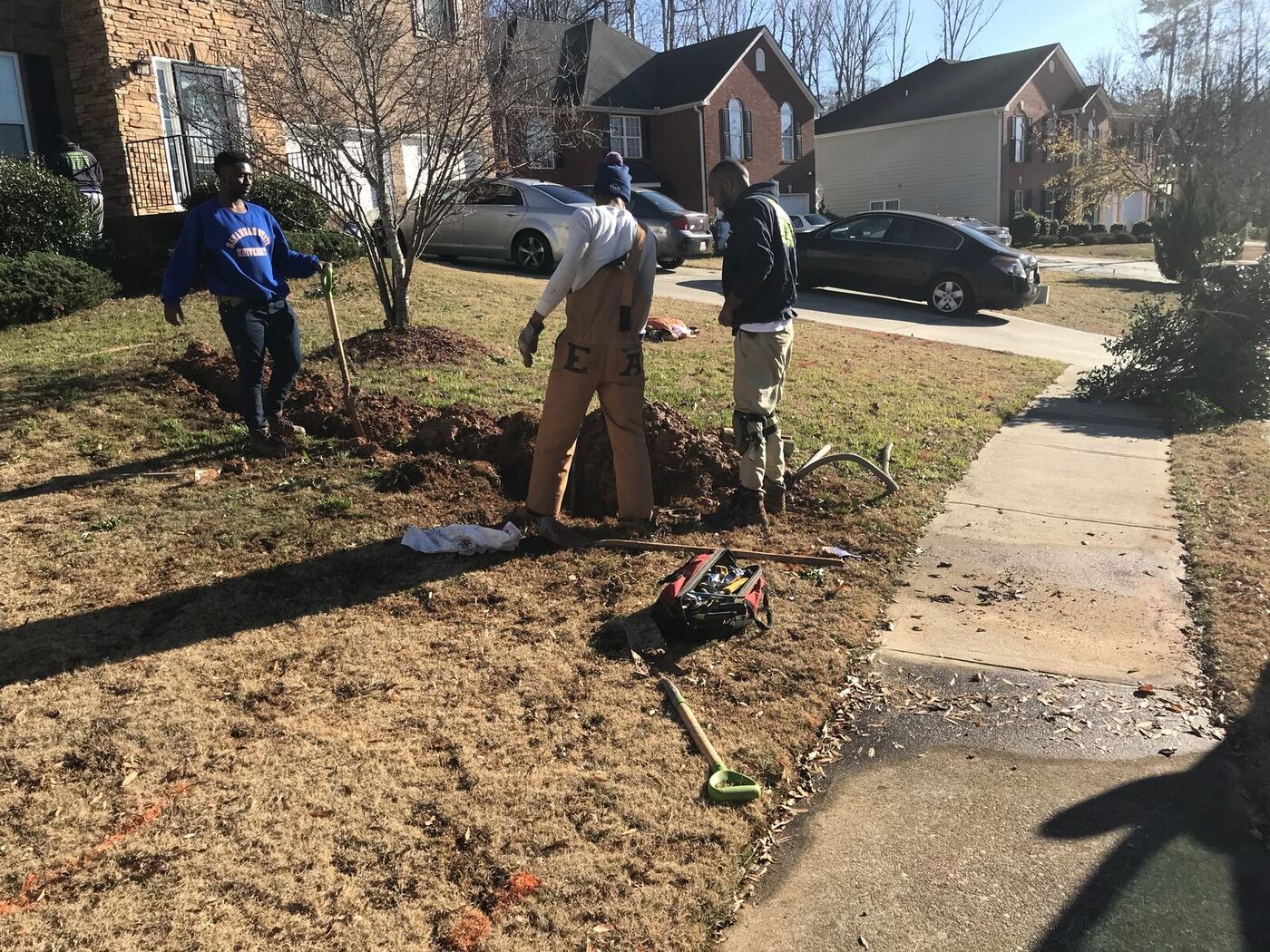Two plumbers digging up a broken water service line in a front yard
